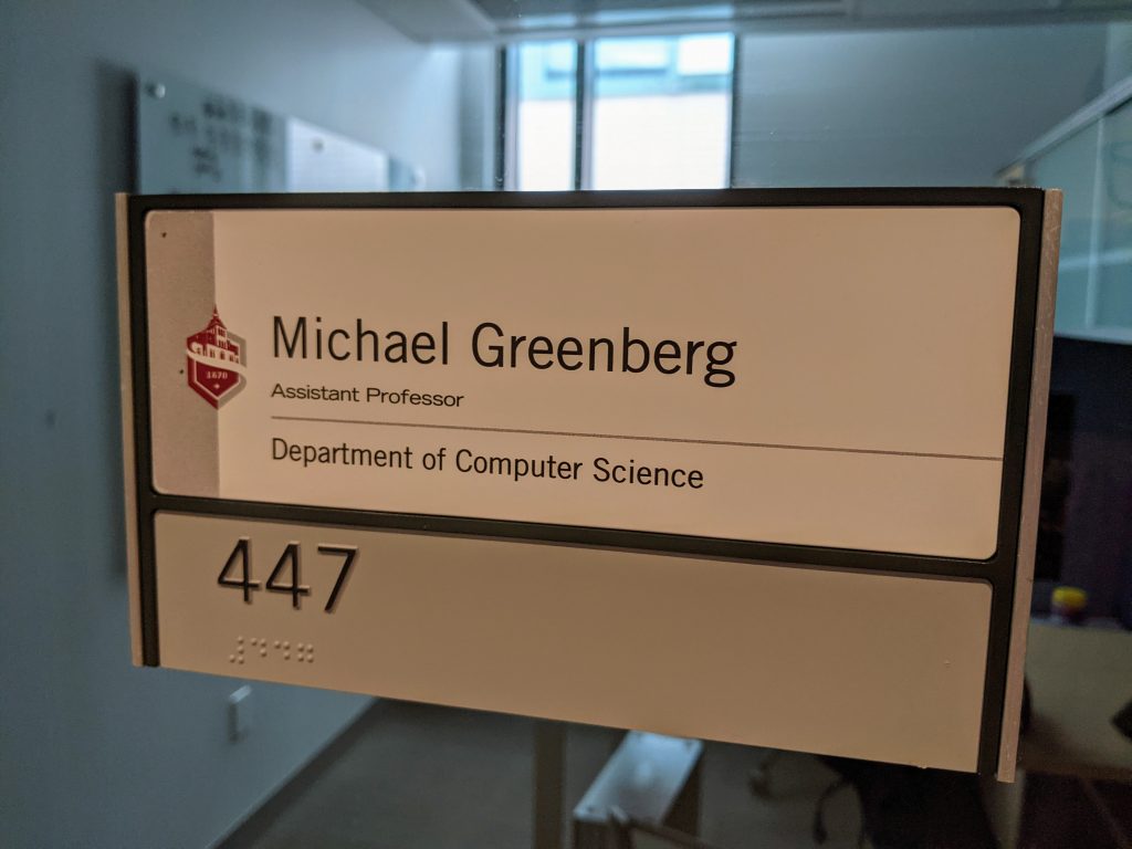 A photo of my office nameplate. The Stevens logo in red, with the following text:

Michael Greenberg
Assistant Professor
Department of Computer Science

447
447 (in Braille)